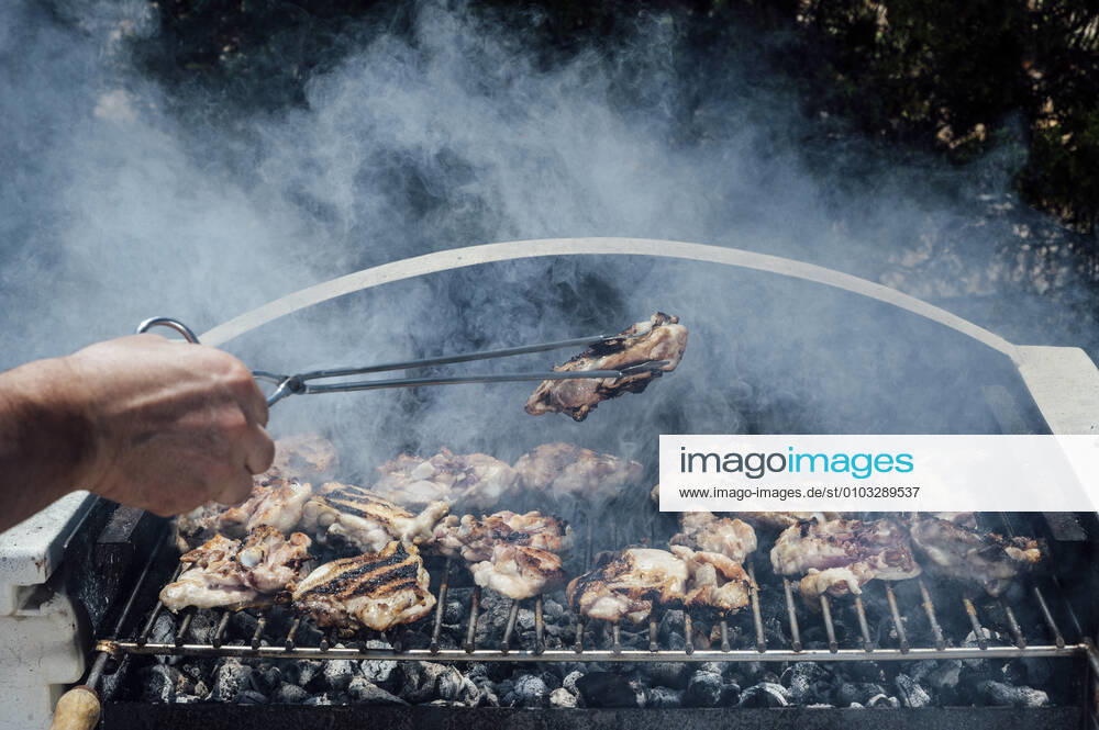 Hand of young man holding meat with serving tongs on barbecue grill in yard model released Symbolfoto JCMF01053