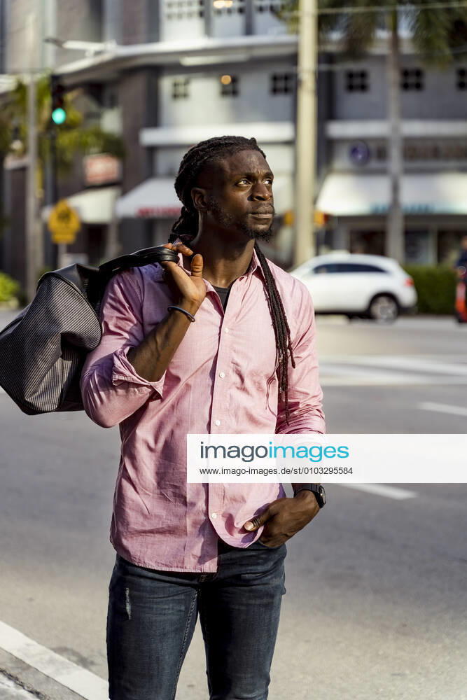 Thoughtful afro young man with bag standing on street in Miami, Florida, USA model released Symbolfoto MAUF03495