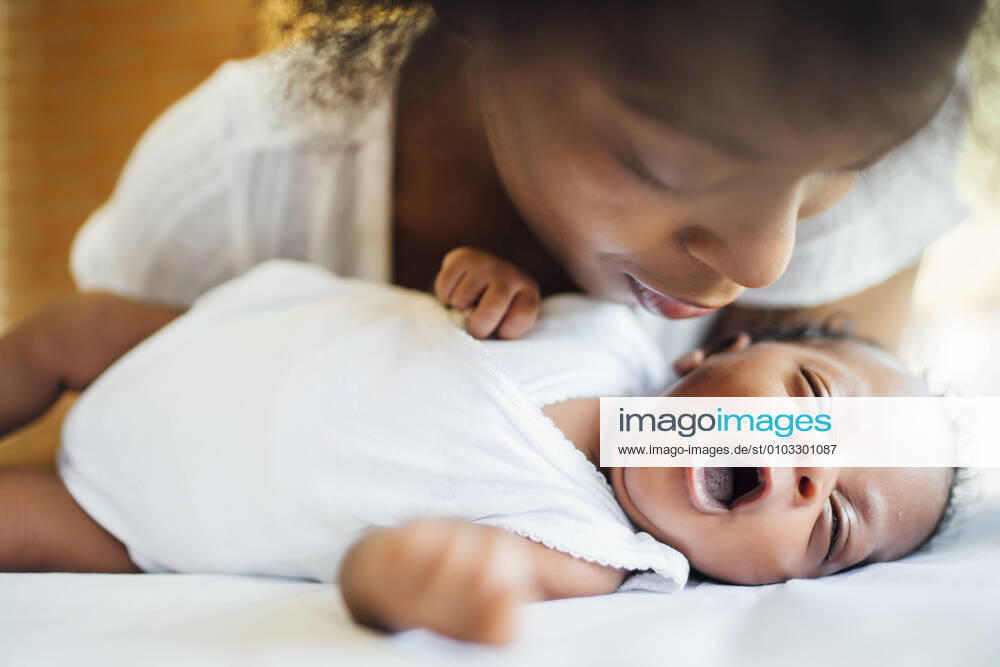 Close-up of mother looking at cute newborn daughter yawning while lying on bed model released Symbolfoto OCMF01536