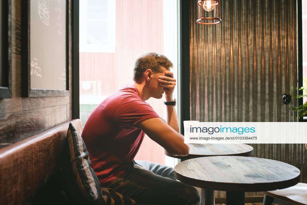 Man sat covering his face feeling stressed whilst sat in a cafe Norrtälje, Stockholm County, Sweden CR_RABE200824-475860-01 ,model released, Symbolfoto