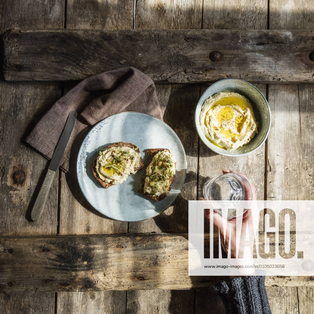 IMAGO Creative, Food, Hummus Hand of woman holding glass of water and plate with bread slices with hummus and sprouts model released Symbolfoto EVGF03726