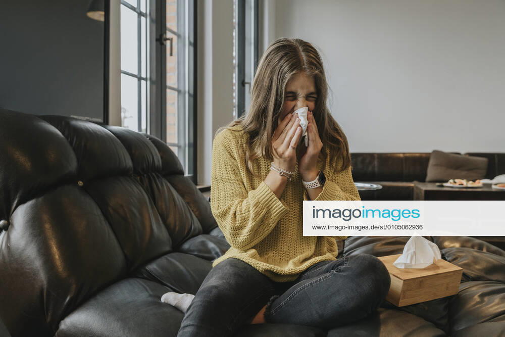 Girl blowing nose while sitting on coach at home model released Symbolfoto property released MFF06191