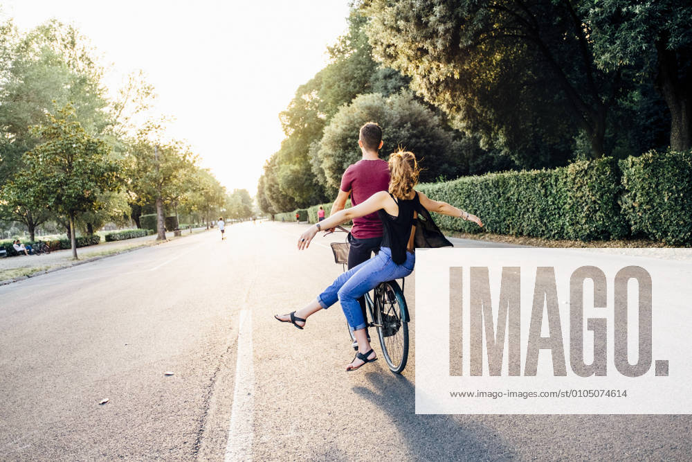 Young woman with arms outstretched sitting with boyfriend on bicycle in park model released Symbolfoto SBAF00032