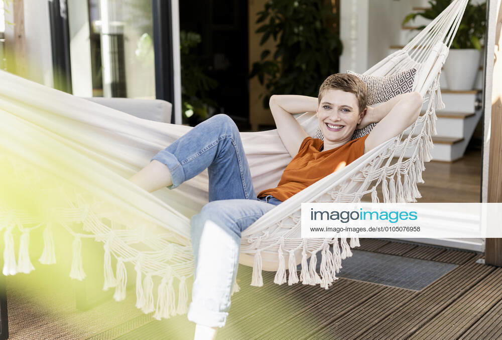 Smiling woman with hands behind head relaxing on hammock against house in yard model released Symbolfoto property released UUF21276