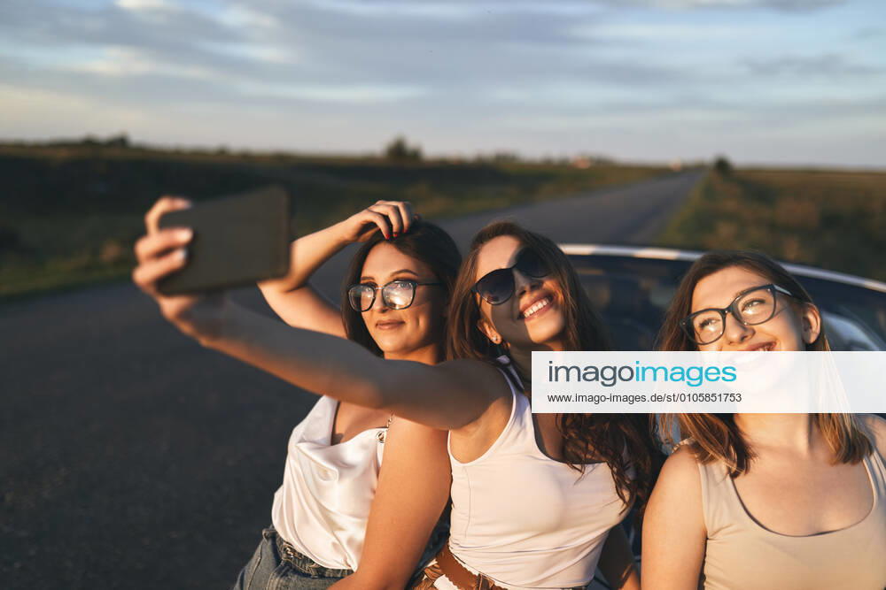 Smiling friends taking selfie while standing on road during sunset model released Symbolfoto ZEDF03820
