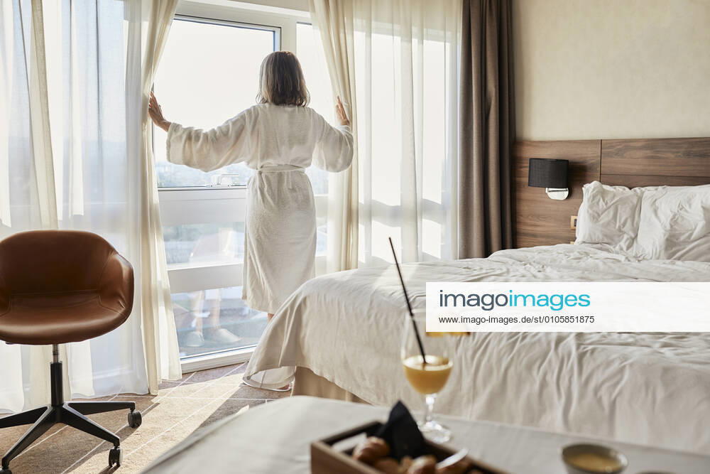 Retired senior woman opening curtain while looking through window at luxury hotel room model released Symbolfoto property released ZEDF03917