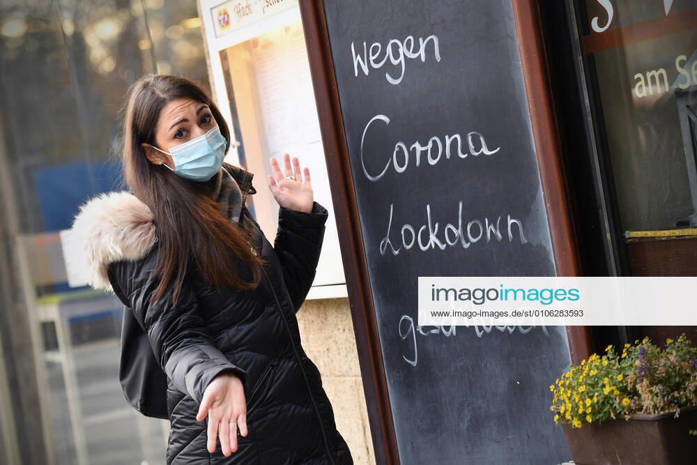 Themenbild: Coronavirus Pandemie Folgen fuer die Gastronomie. Eine Junge Frau steht mit Mundschutz,Maske ratlos vor einem Schild: WEGEN CORONA LOCKDOWN GESCHLOSSEN, Geschlossenes bayerisches Restaurant am Sendlinger Tor in Muenchen. Seit dem 2.November muss wegen dem Lockdown light die Gastronomie geschlossen bleiben, Schliessung-Folge der Corona Pandemie,Lockdown,Shutdown,Inzidenzwert. MODEL RELEASED!