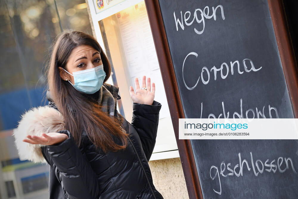 Themenbild: Coronavirus Pandemie Folgen fuer die Gastronomie. Eine Junge Frau steht mit Mundschutz,Maske ratlos vor einem Schild: WEGEN CORONA LOCKDOWN GESCHLOSSEN, Geschlossenes bayerisches Restaurant am Sendlinger Tor in Muenchen. Seit dem 2.November muss wegen dem Lockdown light die Gastronomie geschlossen bleiben, Schliessung-Folge der Corona Pandemie,Lockdown,Shutdown,Inzidenzwert. MODEL RELEASED!