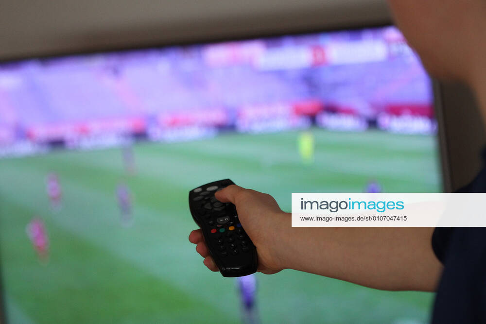 Winden Themenbild - Hand an einer TV-Fernbedienung Themenbild - Hand an einer TV-Fernbedienung Eine Hand haelt im Wohnzimmer, auf der Couch, eine Sky TV-Fernbedienung, Fernbedienung, in der Hand. Im Hintergrund laeuft ein Fussballspiel in Sky auf dem Bildschirm. Symbolbild, Themenbild, Featurebild