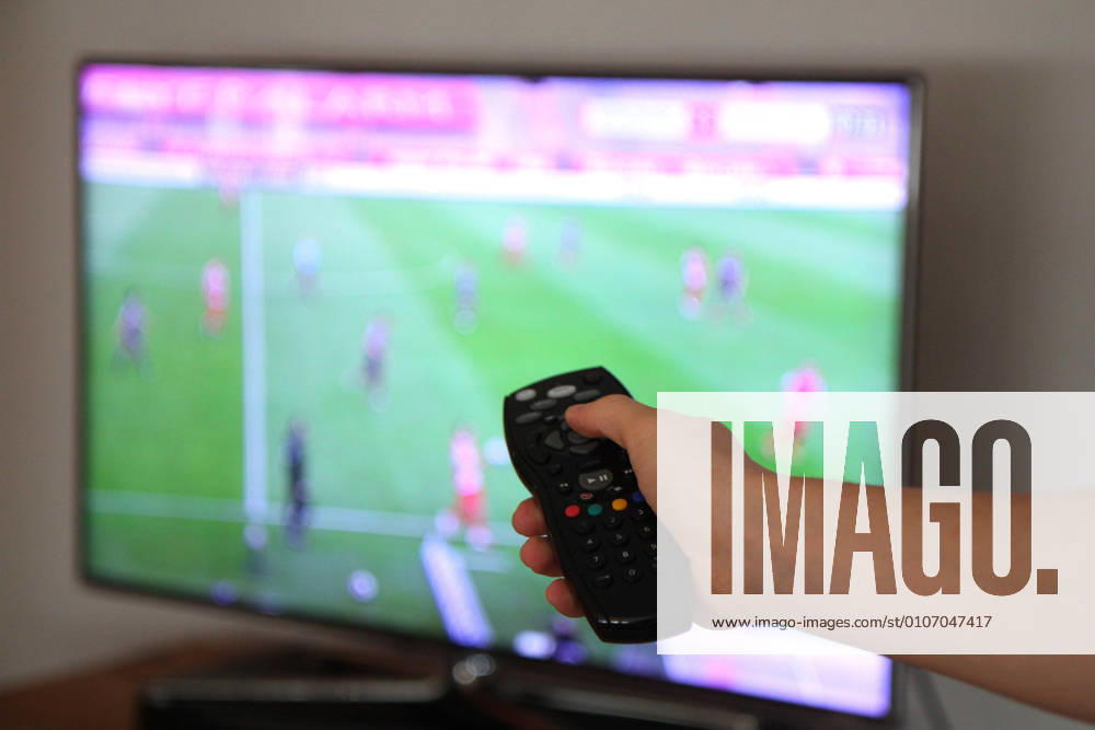 Winden Themenbild - Hand an einer TV-Fernbedienung Themenbild - Hand an einer TV-Fernbedienung Eine Hand haelt im Wohnzimmer, auf der Couch, eine Sky TV-Fernbedienung, Fernbedienung, in der Hand. Im Hintergrund laeuft ein Fussballspiel in Sky auf dem Bildschirm. Symbolbild, Themenbild, Featurebild
