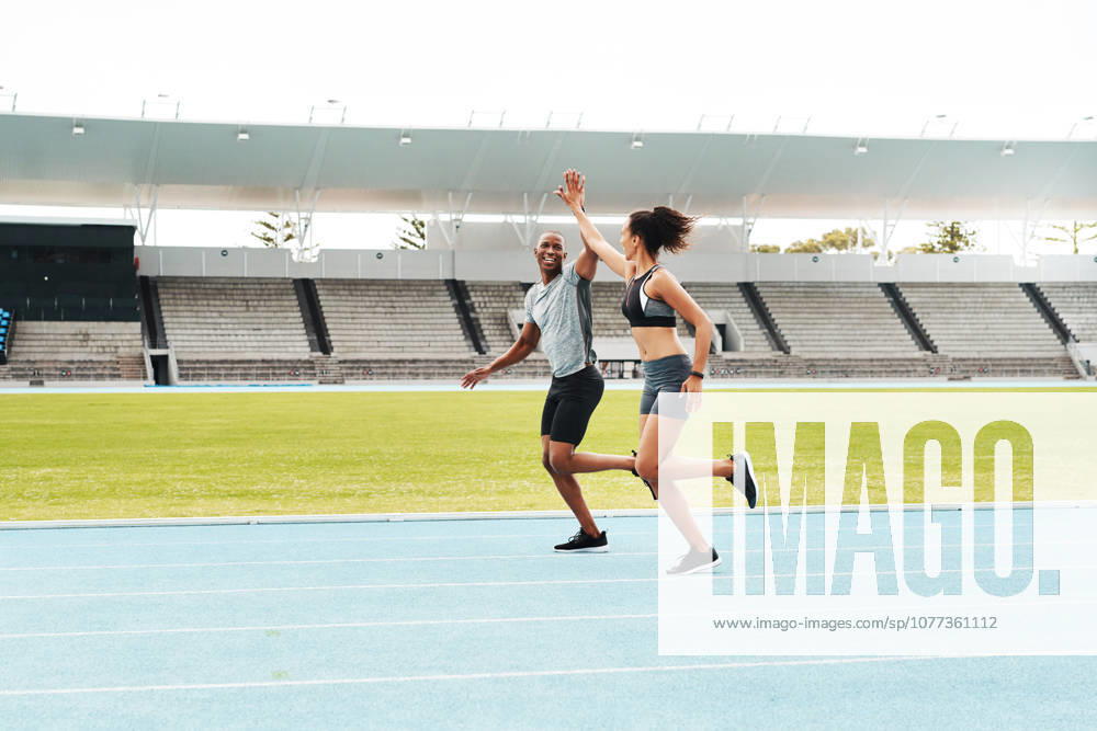 Man, woman and high five for running on track for exercise, fitness and race in stadium. Male athlete, female personal trainer and success in arena for contest, competition and achievement or victory. (License=RF) 21841686 ,model released, Symbolfoto