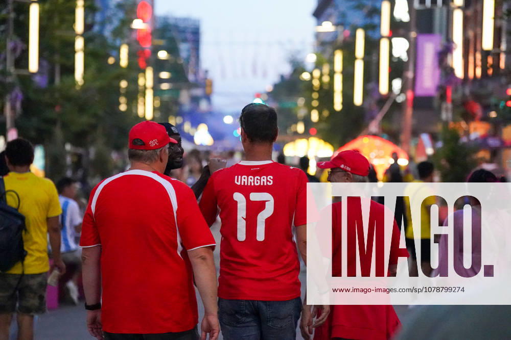 Kanada: Fußball FIFA Weltmeisterschaft 2026 Gruppenphase Schweiz vs Kanada BC Place Stadium (Vancouver, British Columbia): Schweizer Fußballfans in roten Fantrikots und Fanbekleidung auf einer belebten Fußgängerzone am Abend, Rückansicht, Trikot mit Aufschrift Vargas 17, Fanmarsch, Fankultur, Anhänger der Schweizer Nationalmannschaft, Public Viewing Atmosphäre, Freizeit, Reise, Tourismus, Menschenmenge, Straßenleben, Dämmerung, Bokeh-Lichter, Fußballbegeisterung, Supporter, Auswärtsfans, Impression, Symbolfoto.