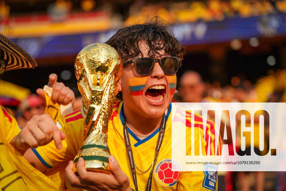 USA: Fußball FIFA Weltmeisterschaft 2026, K.-o.-Runde Sechzehntelfinale (Round of 32) - Kolumbien vs Ghana - Kansas City Stadium (Arrowhead Stadium): Ein begeisterter kolumbianischer Fußballfan im Trikot der Nationalmannschaft jubelt mit einer Nachbildung des FIFA-WM-Pokals. Gesichtsbemalung in den Farben Kolumbiens, Sonnenbrille, Fans, Fankultur, Porträt, Emotionen, Jubel, Zuschauer, Tribüne, Symbolbild.