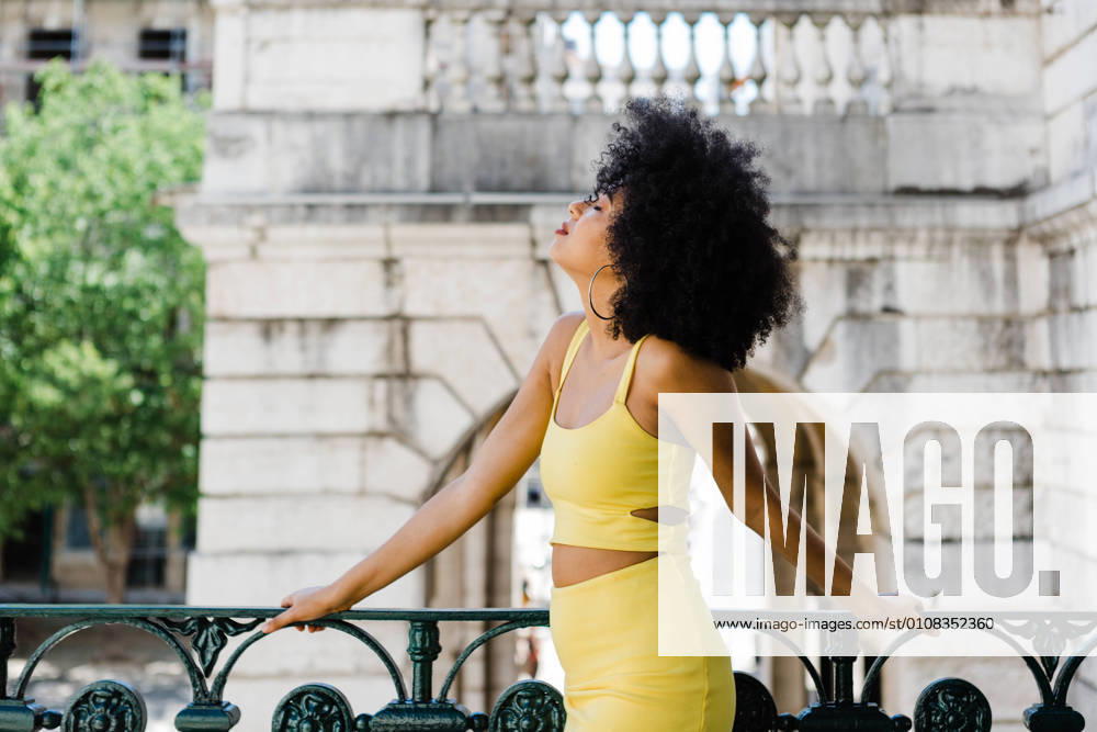 IMAGO Creative: Clickbait, Modetrends Beautiful African American woman in yellow suit and jean jacket standing and looking away on urban background, Model released