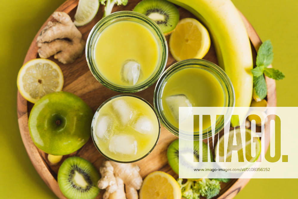 From above of glasses with healthy detox drinks with ice cubes placed on wooden tray with apple and ginger