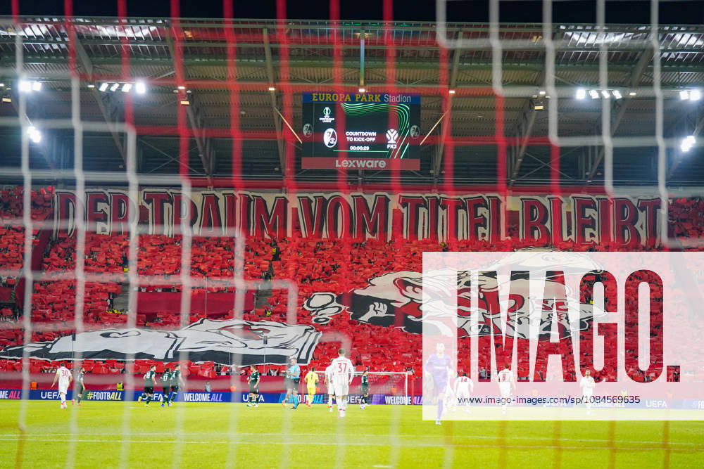 Deutschland: Fussball UEFA Conference League 2026 - 2027, 1. Spieltag - SC Freiburg vs FK Jablonec - Europa-Park-Stadion (Freiburg): Choreographie der Fans des SC Freiburg auf der Südtribüne im Europa-Park-Stadion beim UEFA Conference League-Spiel gegen FK Jablonec. Rote Fan-Choreo mit überdimensionalem Spruchband DER TRAUM VOM TITEL BLEIBT und grosser SC-Freiburg-Motivfahne. Aufnahme aus der Hintertorperspektive durch das Tornetz mit Spielern auf dem Rasen. SC Freiburg, FK Jablonec, Europapokal, Fankultur, Ultras, Fans, Zuschauer, Choreographie, Fanchoreo, Transparent, Stadion, Anzeigetafel, Lexware, Werbung.