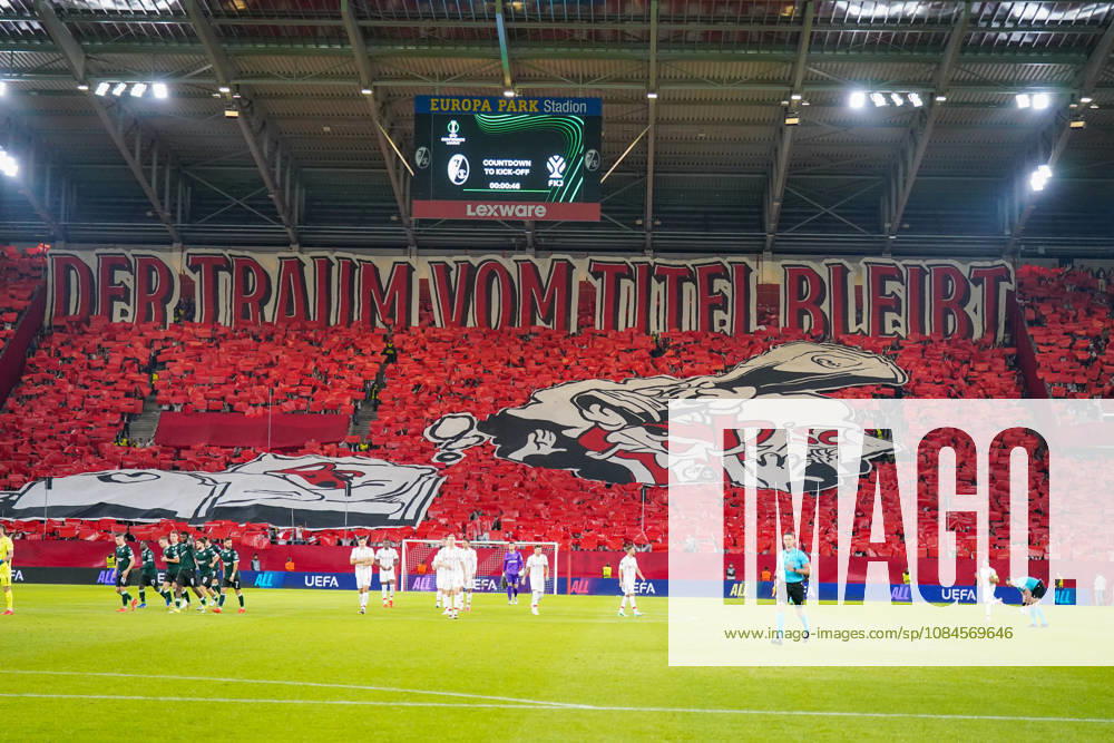 Deutschland: Fussball UEFA Conference League 2026 - 2027, 1. Spieltag - SC Freiburg vs FK Jablonec - Europa-Park-Stadion (Freiburg): Choreographie der Fans des SC Freiburg auf der Südtribüne im Europa-Park-Stadion beim UEFA Conference League-Spiel gegen FK Jablonec. Rote Fan-Choreo mit überdimensionalem Spruchband DER TRAUM VOM TITEL BLEIBT und grosser SC-Freiburg-Motivfahne. Aufnahme aus der Hintertorperspektive durch das Tornetz mit Spielern auf dem Rasen. SC Freiburg, FK Jablonec, Europapokal, Fankultur, Ultras, Fans, Zuschauer, Choreographie, Fanchoreo, Transparent, Stadion, Anzeigetafel, Lexware, Werbung.