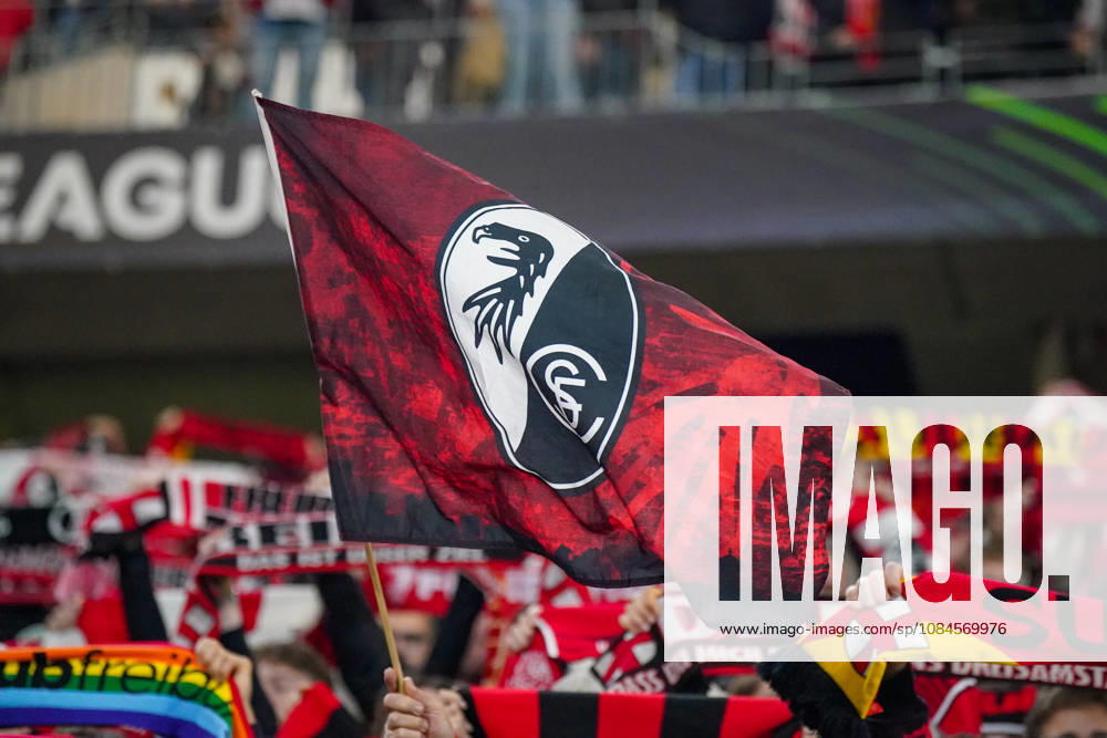 Deutschland: Fussball UEFA Conference League 2026 - 2027, 1. Spieltag - SC Freiburg vs FK Jablonec - Europa-Park-Stadion (Freiburg): Rot-schwarze Fahne mit dem Vereinswappen des SC Freiburg auf der Fantribüne im Europa-Park-Stadion beim UEFA Conference League-Spiel gegen FK Jablonec. Im Hintergrund zahlreiche Anhänger mit hochgehaltenen Fanschals, darunter ein Regenbogenschal. SC Freiburg, FK Jablonec, Fussball, Europapokal, Vereinsfahne, Schwenkfahne, Vereinslogo, Vereinswappen, Fans, Zuschauer, Fankultur, Fanblock, Heimfans, Supporter, Stimmung, Fanartikel, Regenbogen, Vielfalt, Diversität, Toleranz, Stadion.