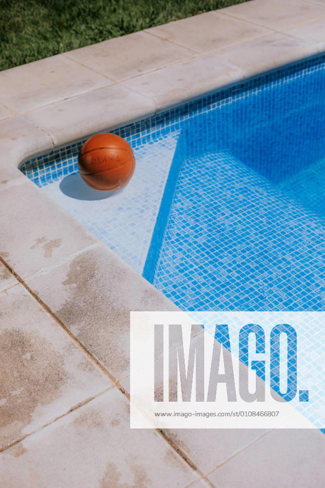From above of basketball ball in corner on swimming pool in terrace of house with green grass