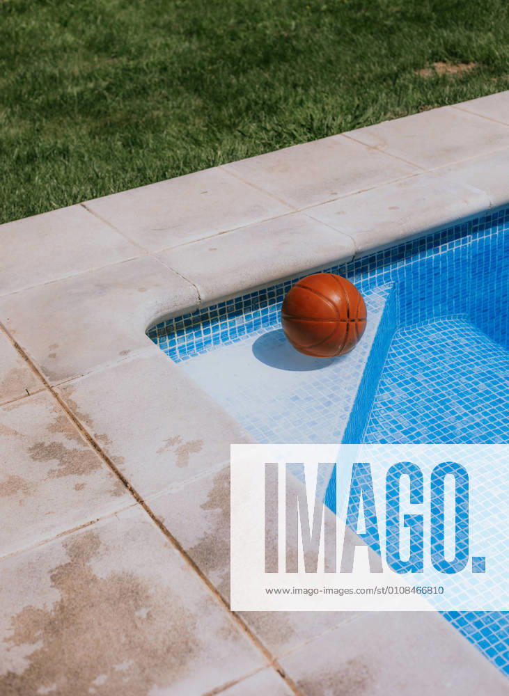 From above of basketball ball in corner on swimming pool in terrace of house with green grass