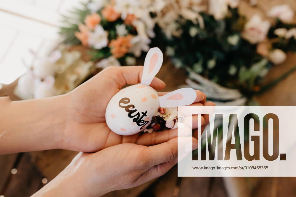Young woman holding an easter egg with rabbit ears painted by children with flowers