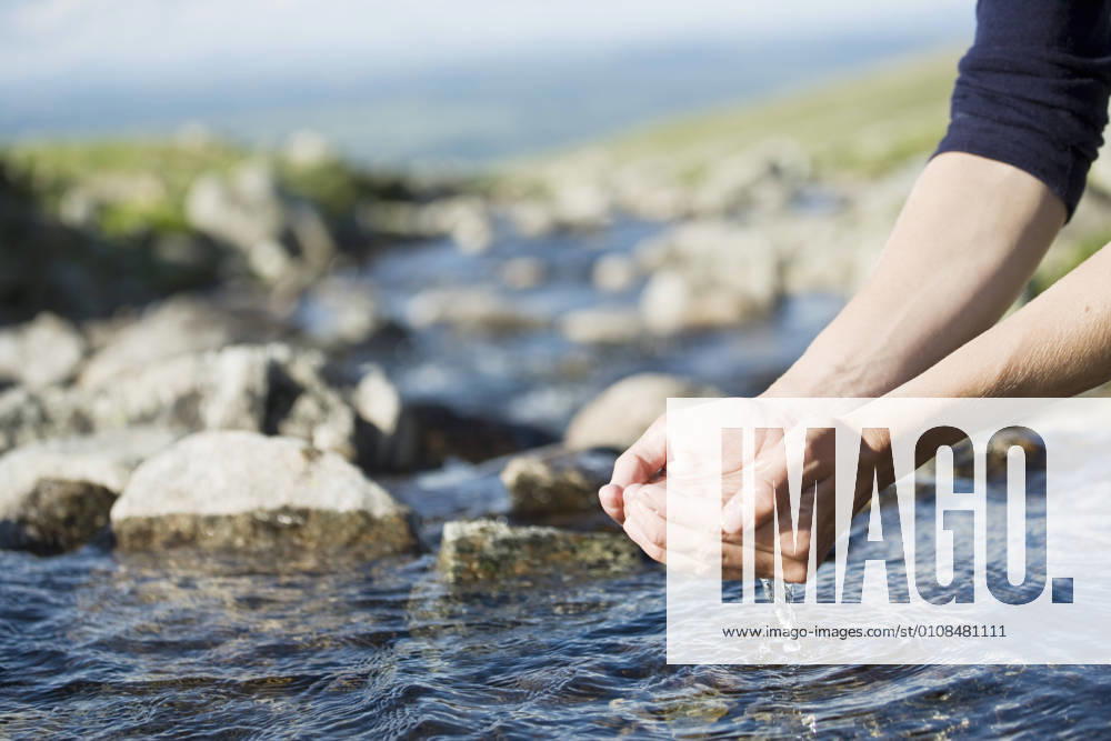 Cropped image of hiker s hands holding water over stream , model released