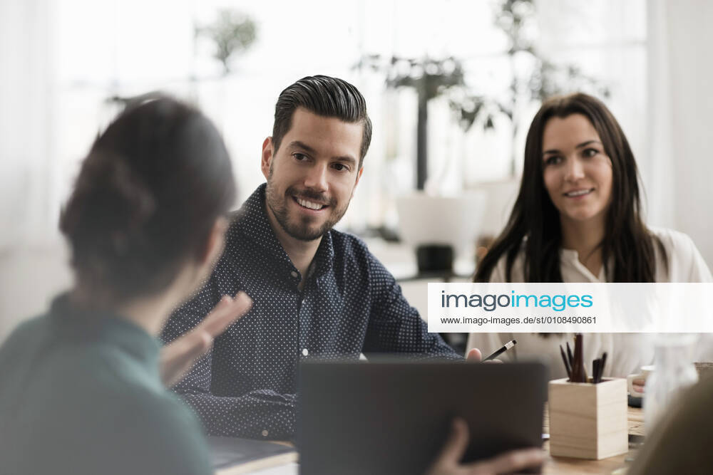Smiling colleagues looking at businesswoman showing laptop during meeting , model released, property released
