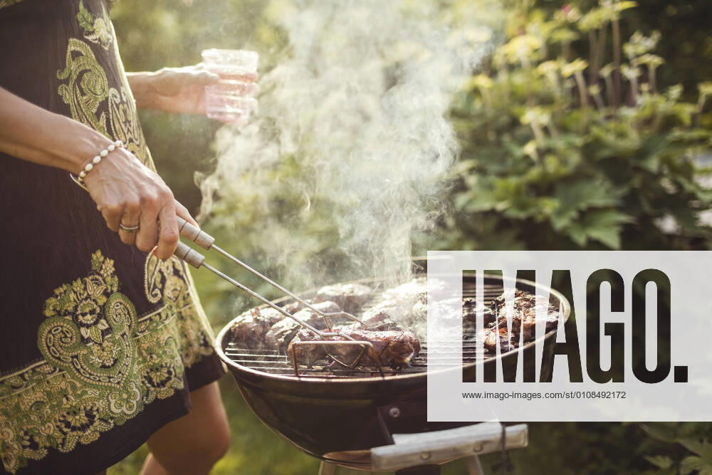 Midsection of woman grilling meat on barbecue in back yard , model released, property released