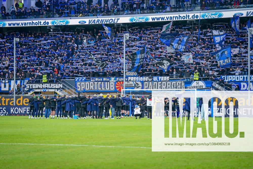 Deutschland: Fussball Bundesliga 2026 - 2027, 7. Spieltag - SC Paderborn vs Hamburger SV - Home-Deluxe-Arena (Paderborn): Heimsieg des SC Paderborn 07 gegen den Hamburger SV (HSV). Spieler, Trainer und Betreuer feiern nach Spielende gemeinsam mit den Heimfans vor der Fankurve der Home-Deluxe-Arena. Siegesfeier, Jubel, Mannschaft, Mannschaftsfoto von hinten, Schulterschluss, Fans, Ultras, Zuschauer, Tribüne, Fahnen, Schals, Fangesänge, Emotionen, Bundesliga, Fussball, Heimsieg, Sportstätte, Innenansicht, Totale, Hintertorperspektive, Tor, Fanbanner, Fankultur, Zusammenhalt.