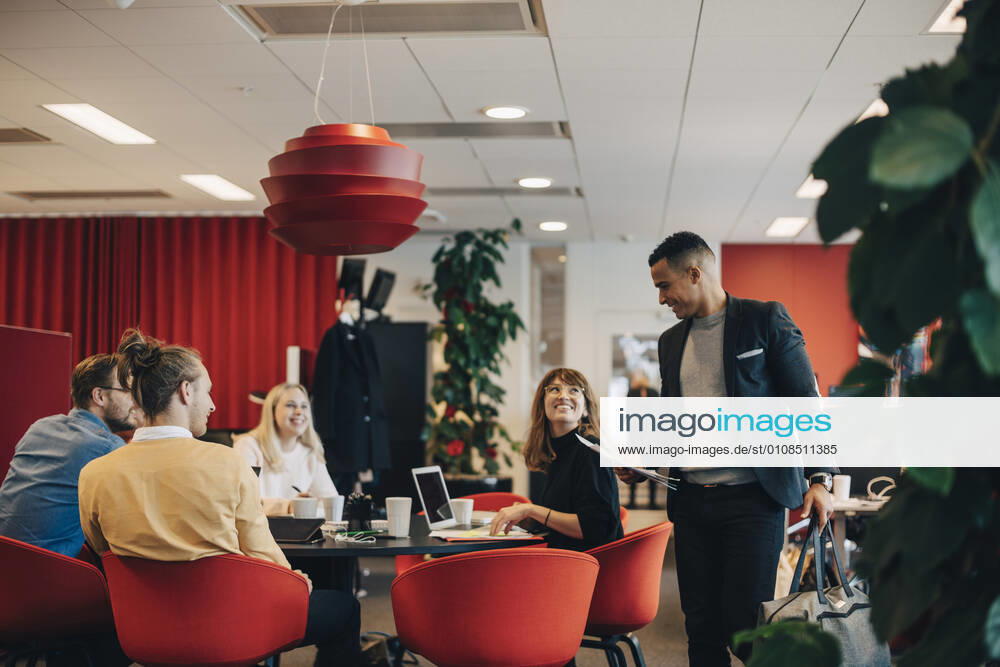 Smiling colleagues looking at businessman standing with bag and documents at office , model released, property released