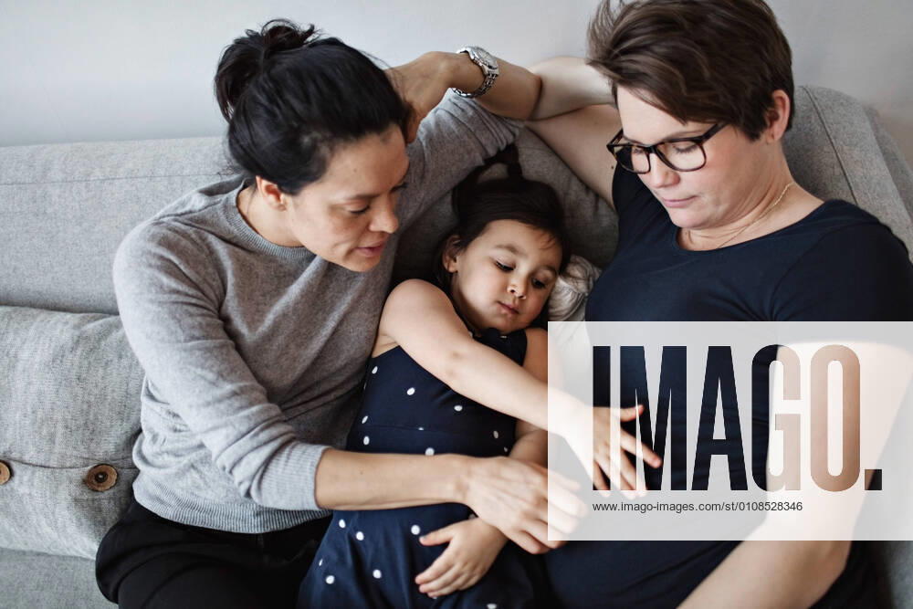IMAGO Creative: Pride Month 2022, Engagement der Jugendlichen IMAGO Creative: Pride Month, Juni 2022, Pärchen und Familien High angle view of mother and daughter touching woman s abdomen while leaning on sofa at home , model released, property released