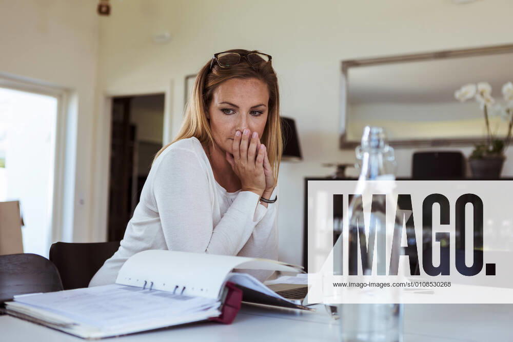 Tensed woman looking at bills while sitting at table in living room , model released, property released