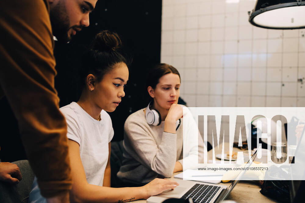 Confident young multi-ethnic colleagues discussing over laptop at office , model released, property released