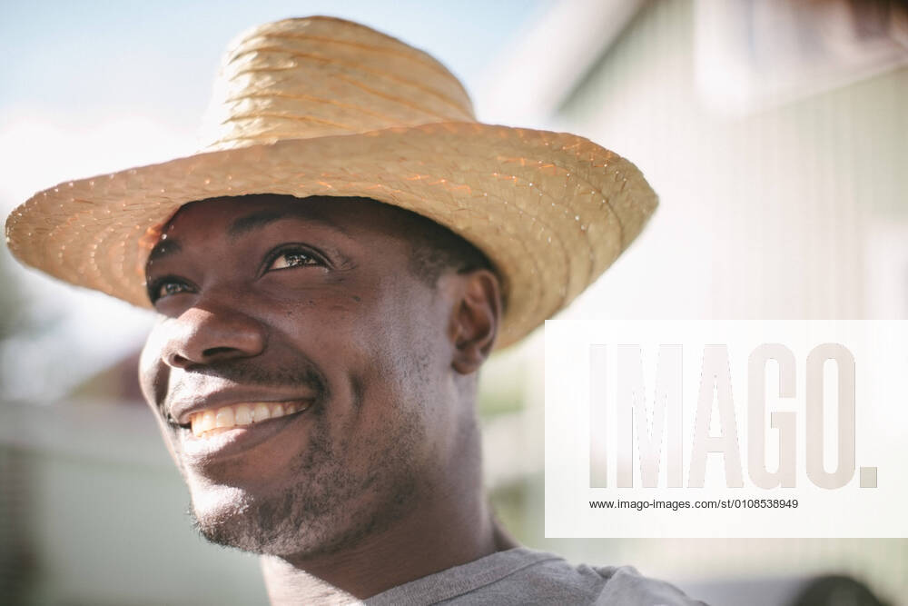 Smiling mid adult man looking away while wearing straw hat during garden party , model released, property released