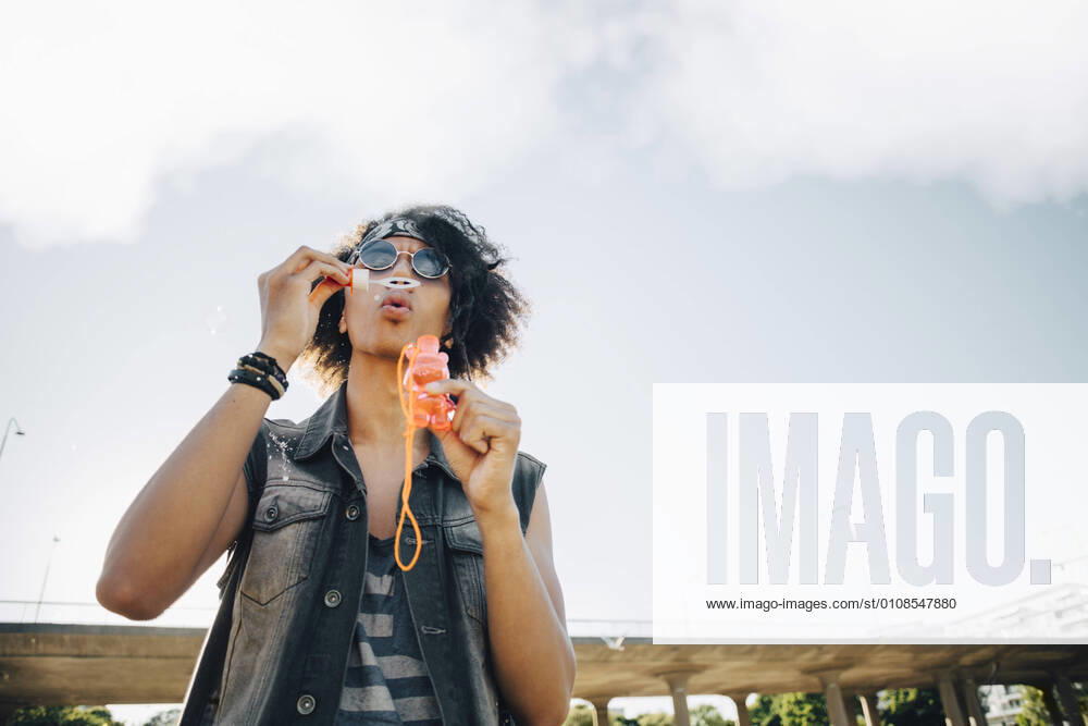 Low angle view of young man blowing soap bubbles against sky , model released