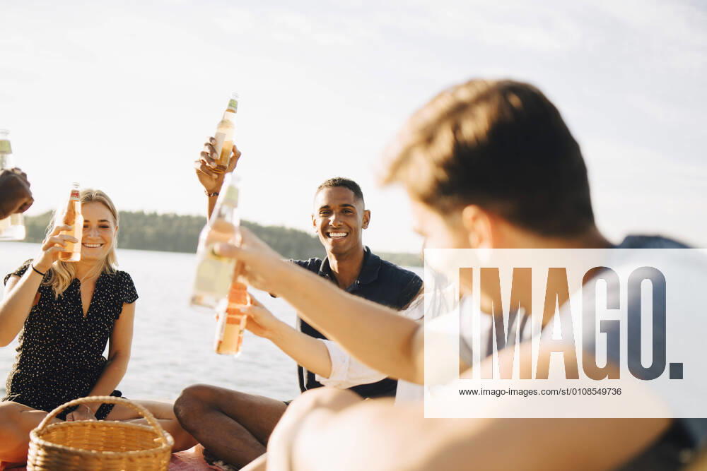 IMAGO Creative: Landleben - Essen Friends enjoying drinks while sitting on jetty against sky in summer , model released