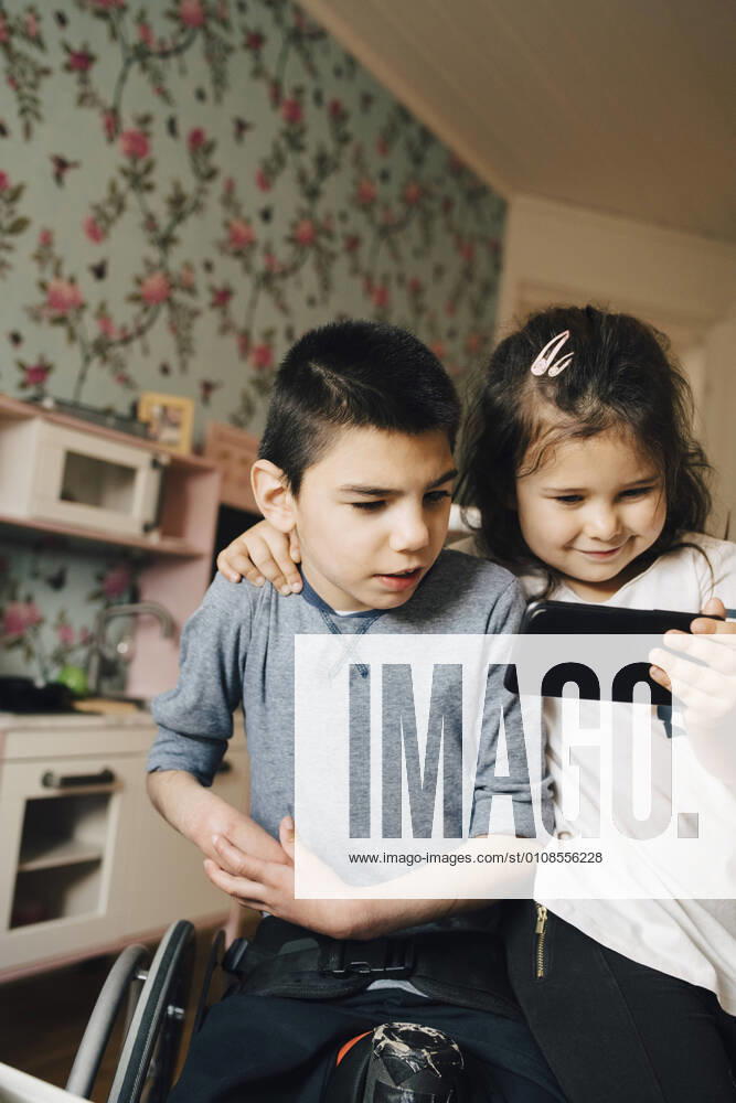 IMAGO Creative: Jahreszeit Winter, Fantasievoll drinnen spielen Sister showing video to autistic brother on smart phone at home , model released, property released