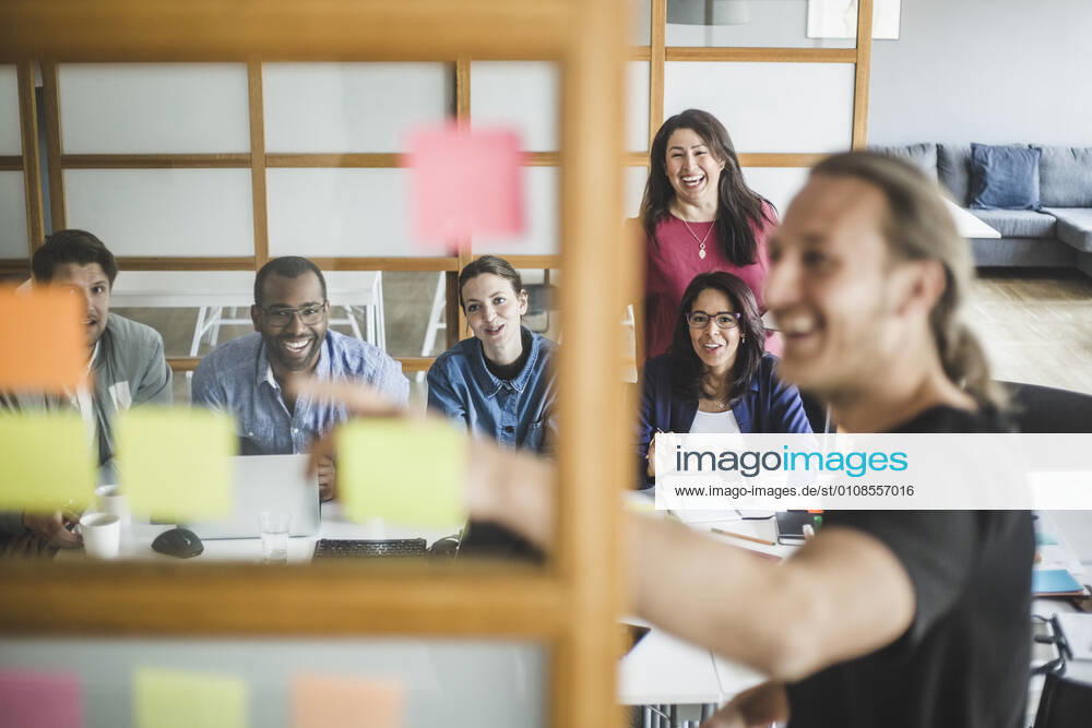 Smiling colleagues looking at businessman explaining strategy in meeting seen through glass wall , model released, property released