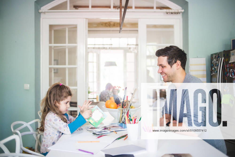 IMAGO Creative: Jahreszeit Winter, Fantasievoll drinnen spielen Smiling father looking at girl holding picture book in kitchen , model released, property released