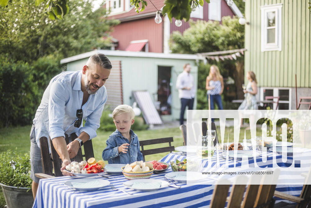 IMAGO Creative: Landleben - Essen Father talking to son while arranging food plate on table in backyard , model released, property released