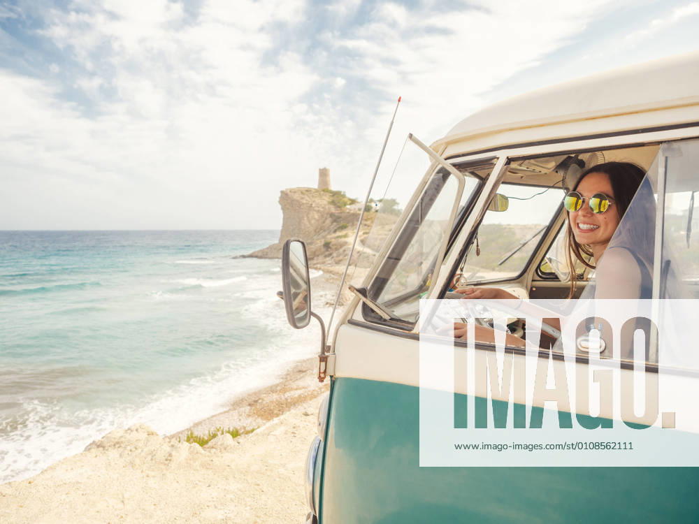 Side view of car with woman drawing on sandy empty beach with foamy waves in bright sunny day