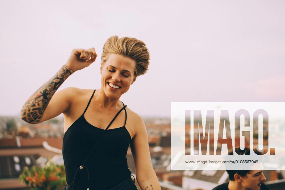 IMAGO Kreativ: Urbane Kultur - Sommer auf den Dächern Excited woman dancing while enjoying with friend on terrace against sky , model released, property released