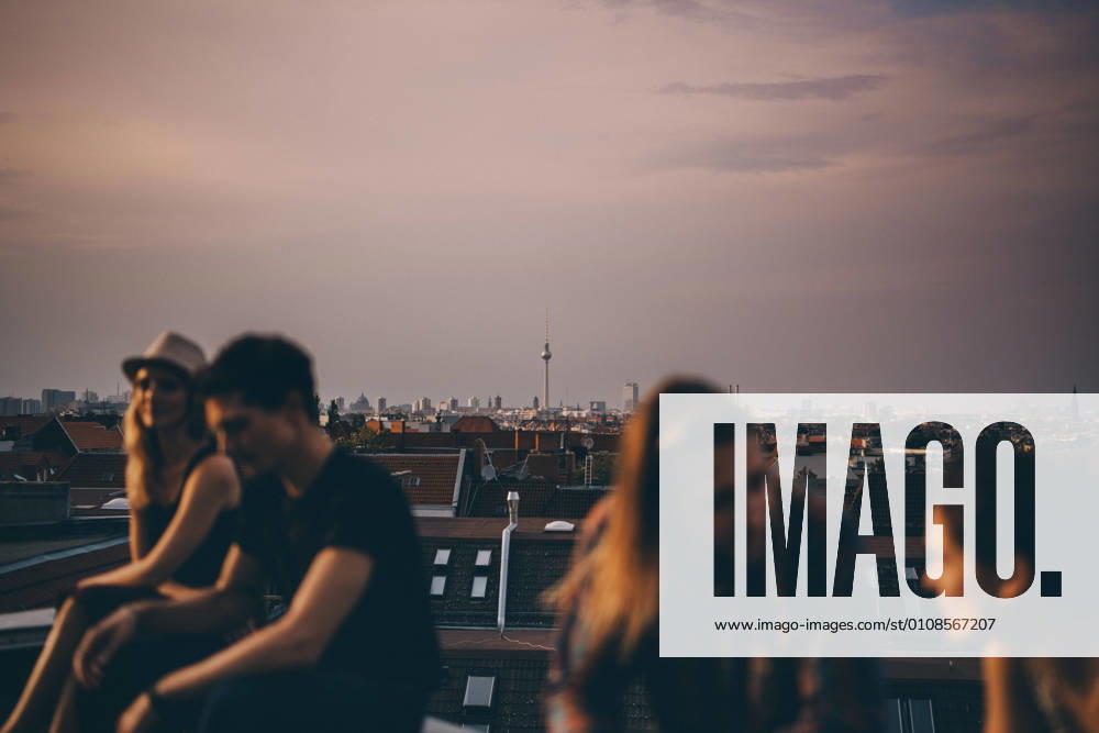 IMAGO Kreativ: Urbane Kultur - Sommer auf den Dächern Friends talking while sitting on terrace during rooftop party in city at dusk , model released, property released