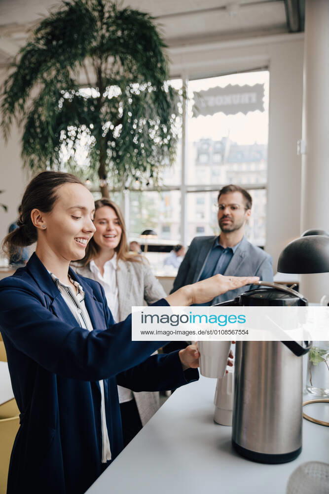 Smiling colleagues looking at businesswoman having coffee during break , model released, property released