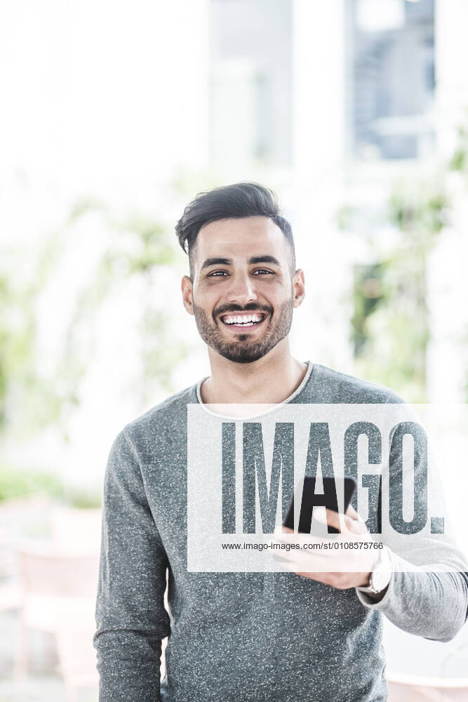 Portrait of smiling businessman holding mobile phone while standing in office , model released, property released