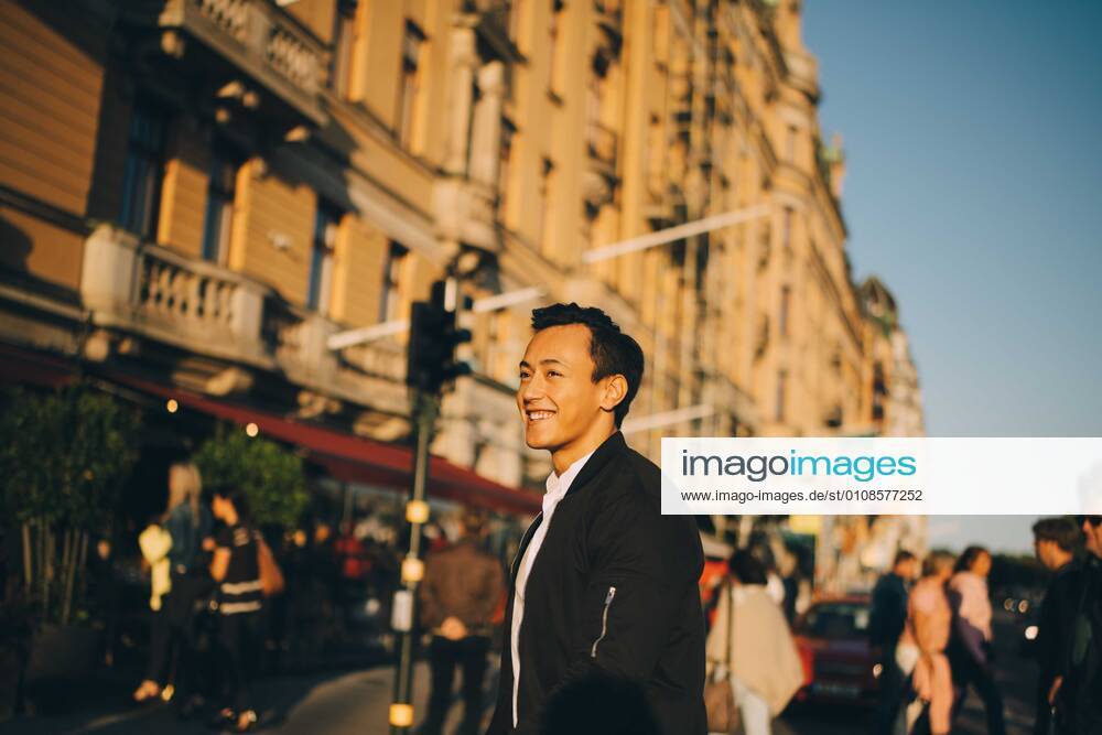 Smiling man looking away while standing against building in city , model released