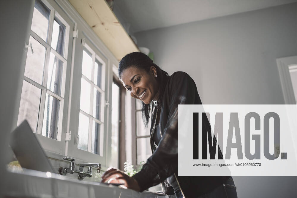 IMAGO Creative: Kreative Renaissance -- der junge Entrepreneur Smiling female professional looking at laptop while standing at home office USA, Los Angeles, model released, property released