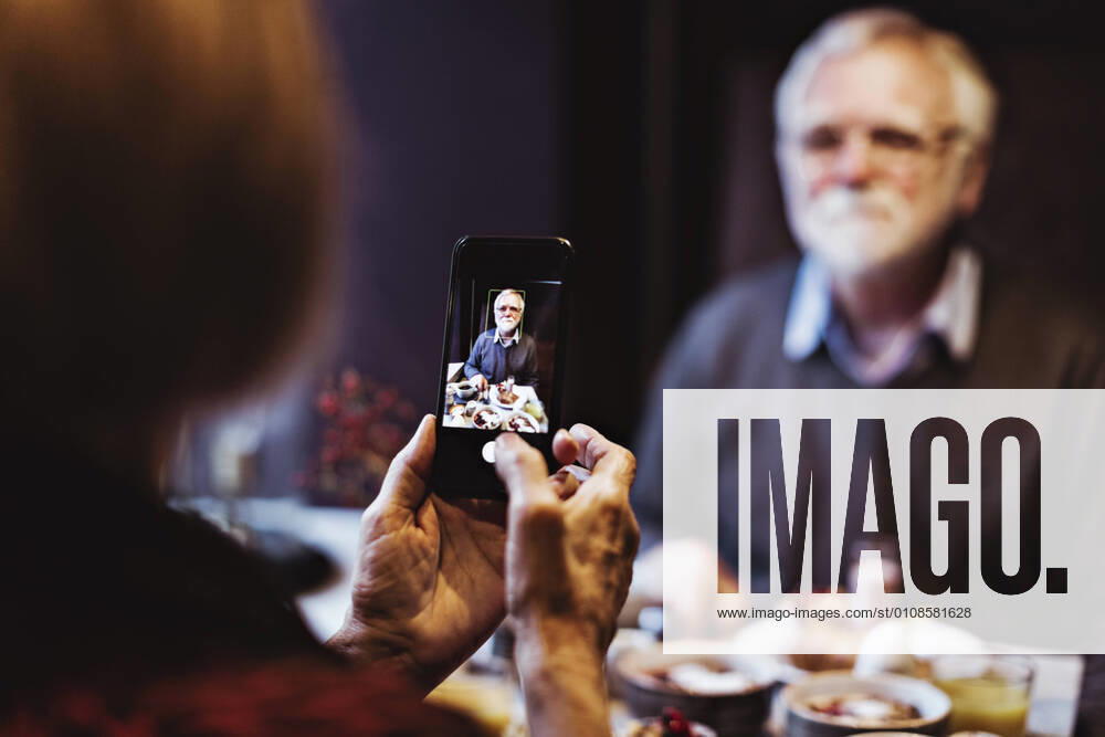IMAGO Creative: Dichotomien, Generationen IMAGO Creative: Landleben - Essen Senior woman photographing man through smart phone while having breakfast at table in hotel Sweden, Stockholm, model released, property released