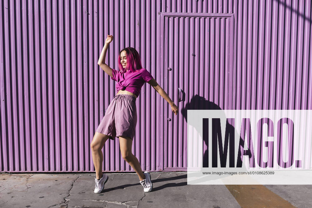 Young woman with dyed red hair dancing in front of purple wall in the city model released Symbolfoto TCEF00994