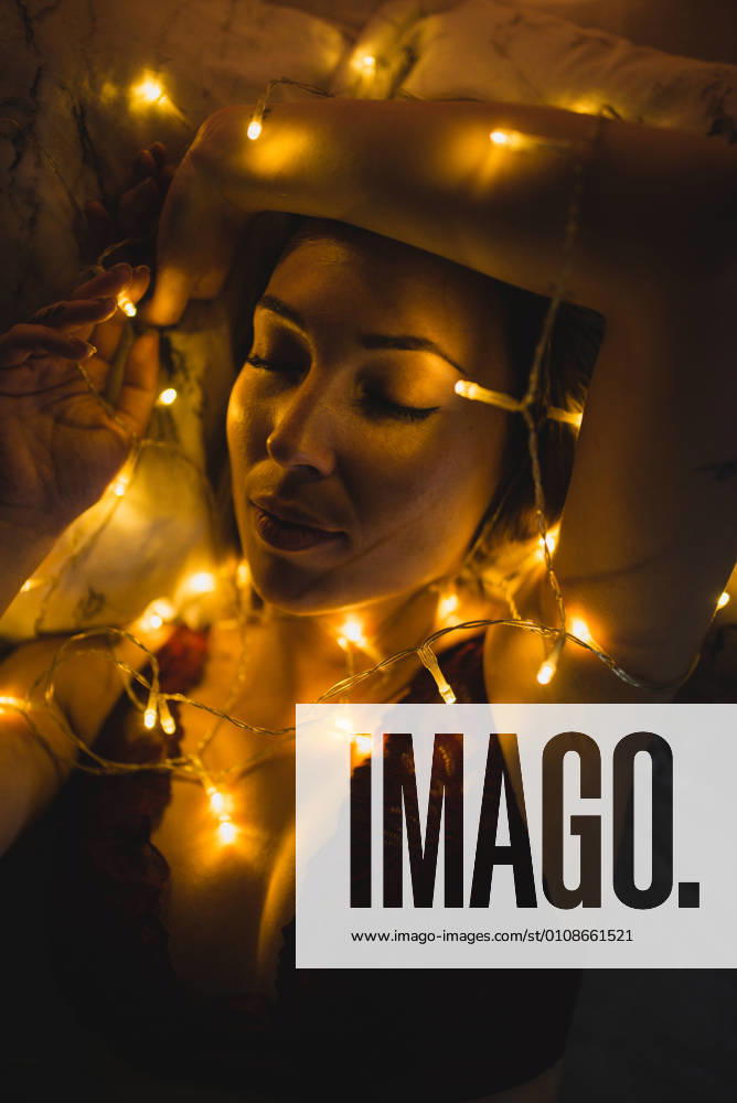 From above young beautiful woman in underwear lying in bed surrounded by light garland, Model released